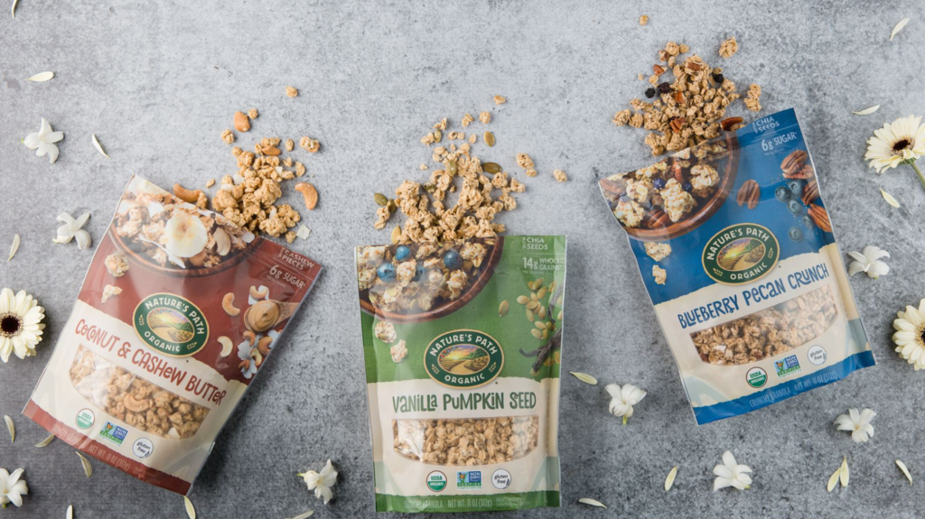 An image showcasing three varieties of Nature's Path granola: coconut and cashew butter, vanilla pumpkin seed, and blueberry pecan crunch. The granola is displayed in small piles, highlighting the texture and ingredients of each flavor.