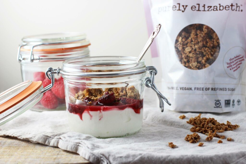 An image depicting a yogurt parfait made with Purely Elizabeth oats, featuring a purple package prominently displayed. The parfait is beautifully layered with creamy yogurt, vibrant fruits, and crunchy granola, showcasing the brand's delicious and nutritious oat products in a visually appealing presentation.