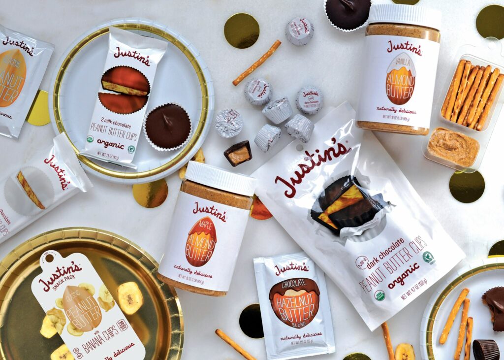An image of Justin's products presented on elegant gold plates arranged on a pristine white table. The assortment includes nut butter jars and snack bars, highlighting the brand's premium offerings in a stylish and inviting setting.