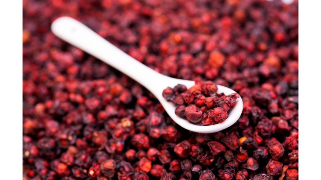 Schisandra berries arranged in a pile with a white spoon resting on top, filled with more berries. The vibrant red berries contrast against the white background, showcasing their rich color and texture.