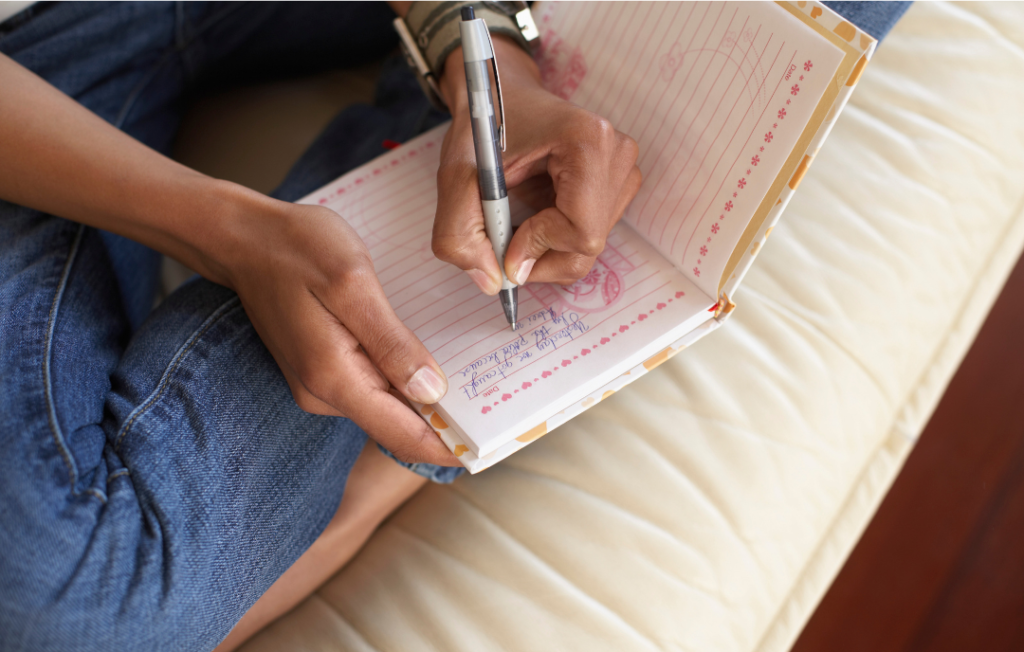 Woman sitting on a white cushion, writing in a journal