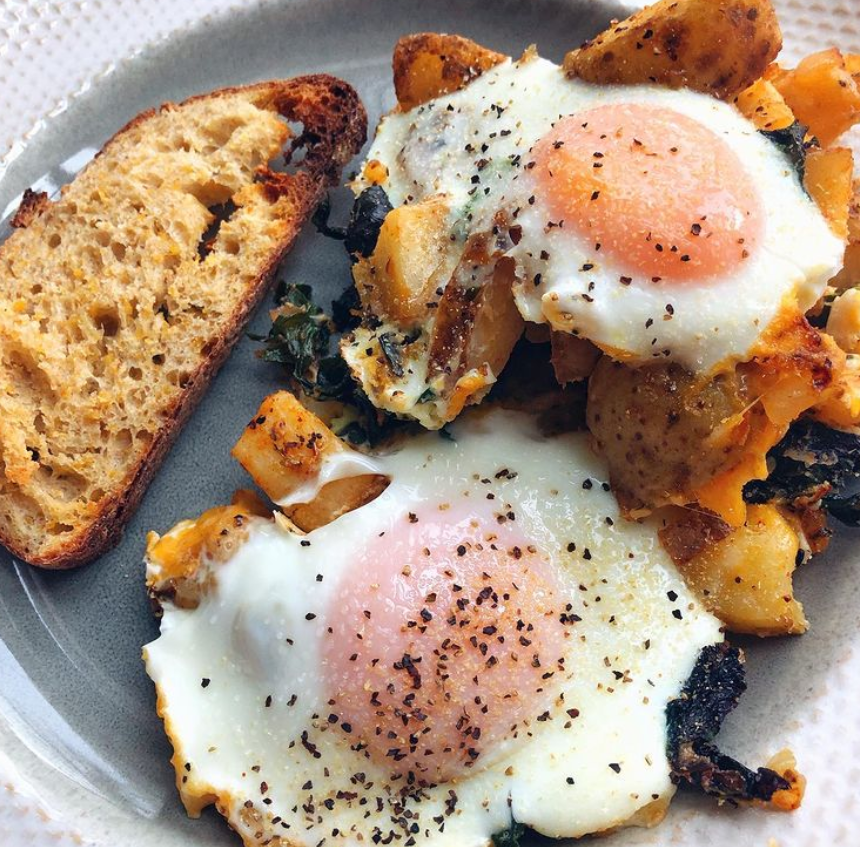 Delicious breakfast plate featuring fried eggs, crispy breakfast potatoes, sautéed spinach, and wheat toast, garnished with salt and pepper, served on a white plate.