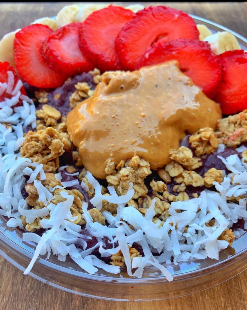 An acai bowl generously topped with vibrant strawberries, coconut flakes, crunchy granola, sliced bananas, and a dollop of creamy peanut butter