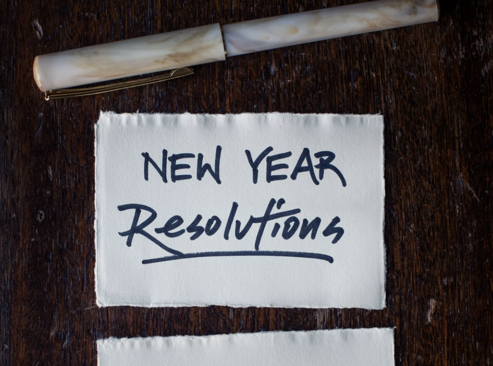 White paper that says "New Year Resolutions" on a table with a pen on top