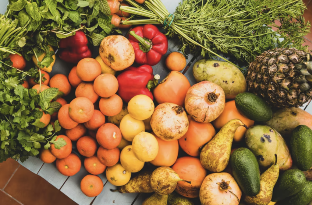 Fresh fruits, vegetables, and herbs on a grey wooden table with a tile background